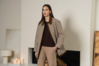 Frau in beiger Jacke, beiger Hose und schwarzem Pullover im Wohnzimmer