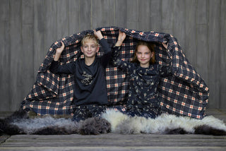 Zwei Kinder in Pyjamas mit Ski-Motiven unter einer Karo-Decke.