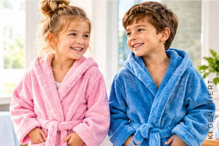 Lachendes Mädchen in einem rosa Bademantel und ein lächelnder Junge in einem blauen Bademantel
