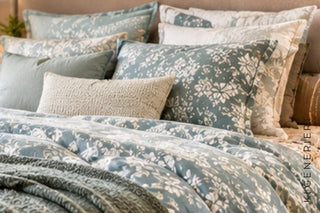 Mehrere Kissen in Salbeigrün und Beige in einem gemütlich gemachten Bett